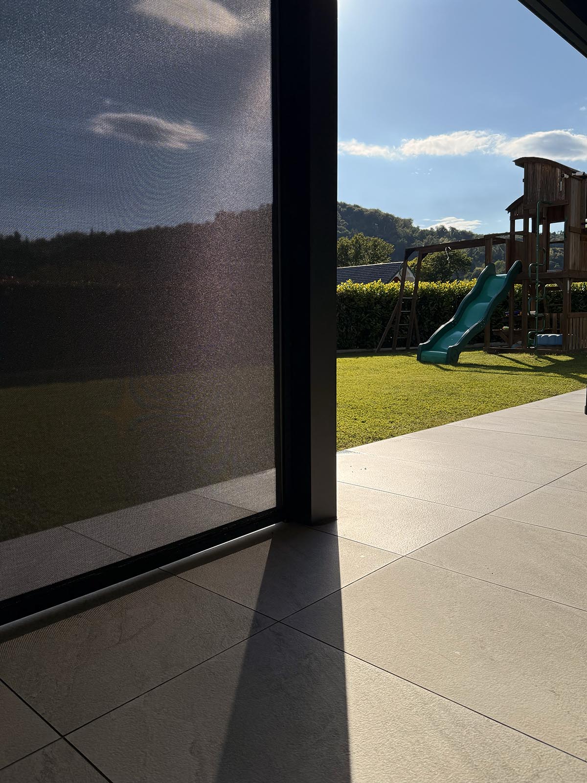 ZIP Screen Roloji Misteral na sodobni terasi z razgledom na zelenico in otroško igralo v ozadju.